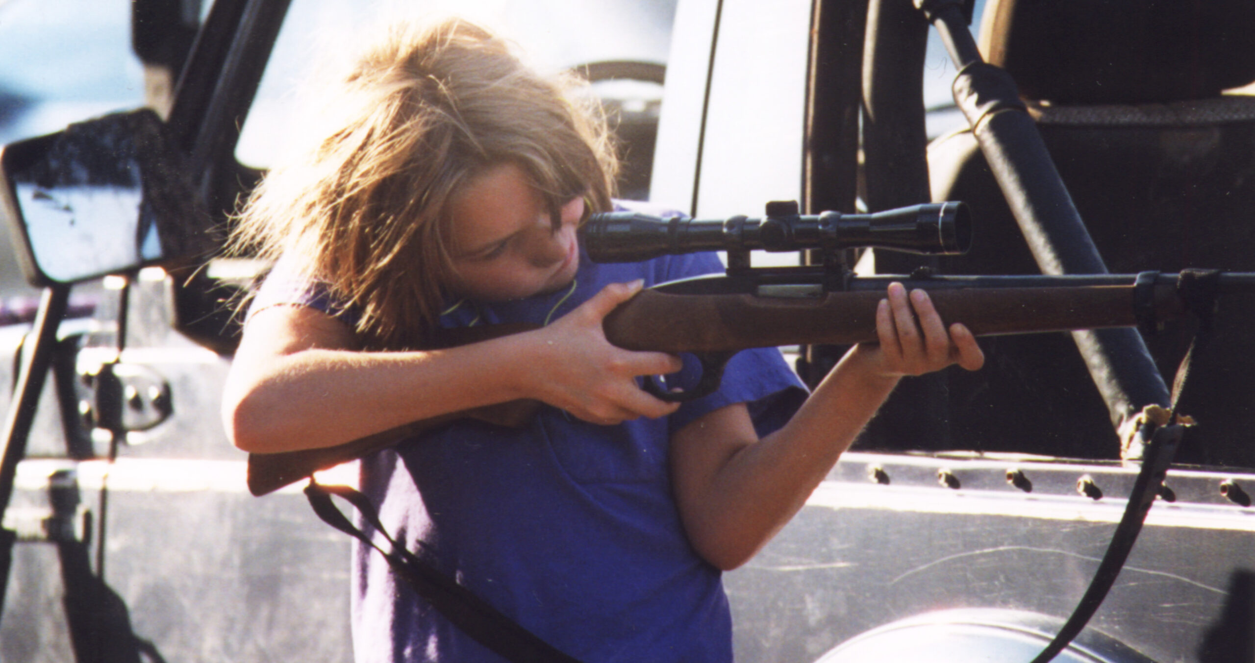 a young girl shooting a large gun with telescopic sight