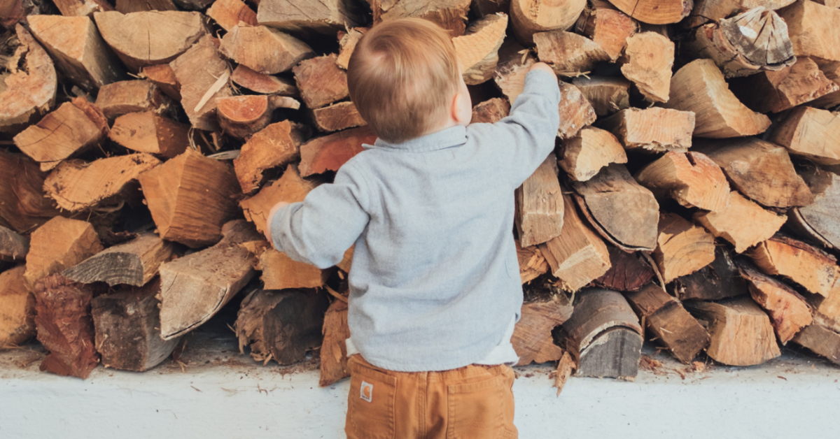 a child reaching for a log in a stack of logs