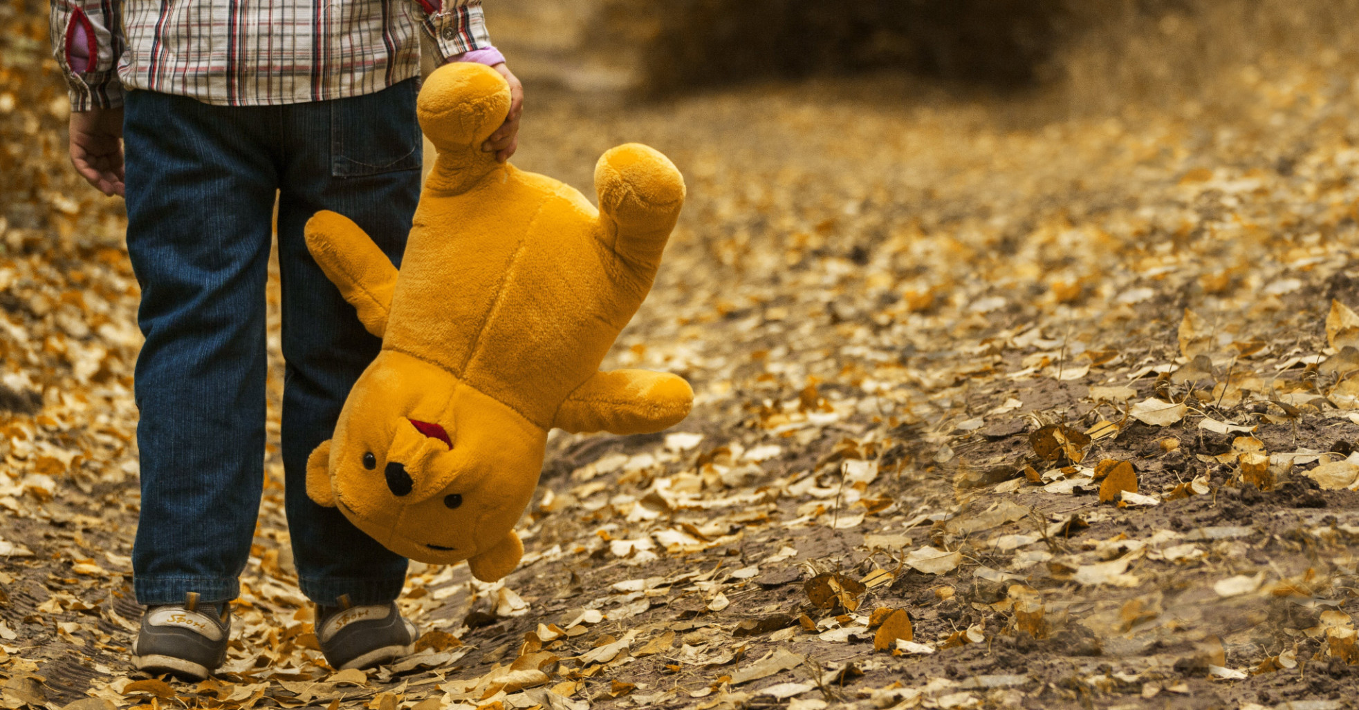 child carrying Winnie the Pooh teddy bear by the leg