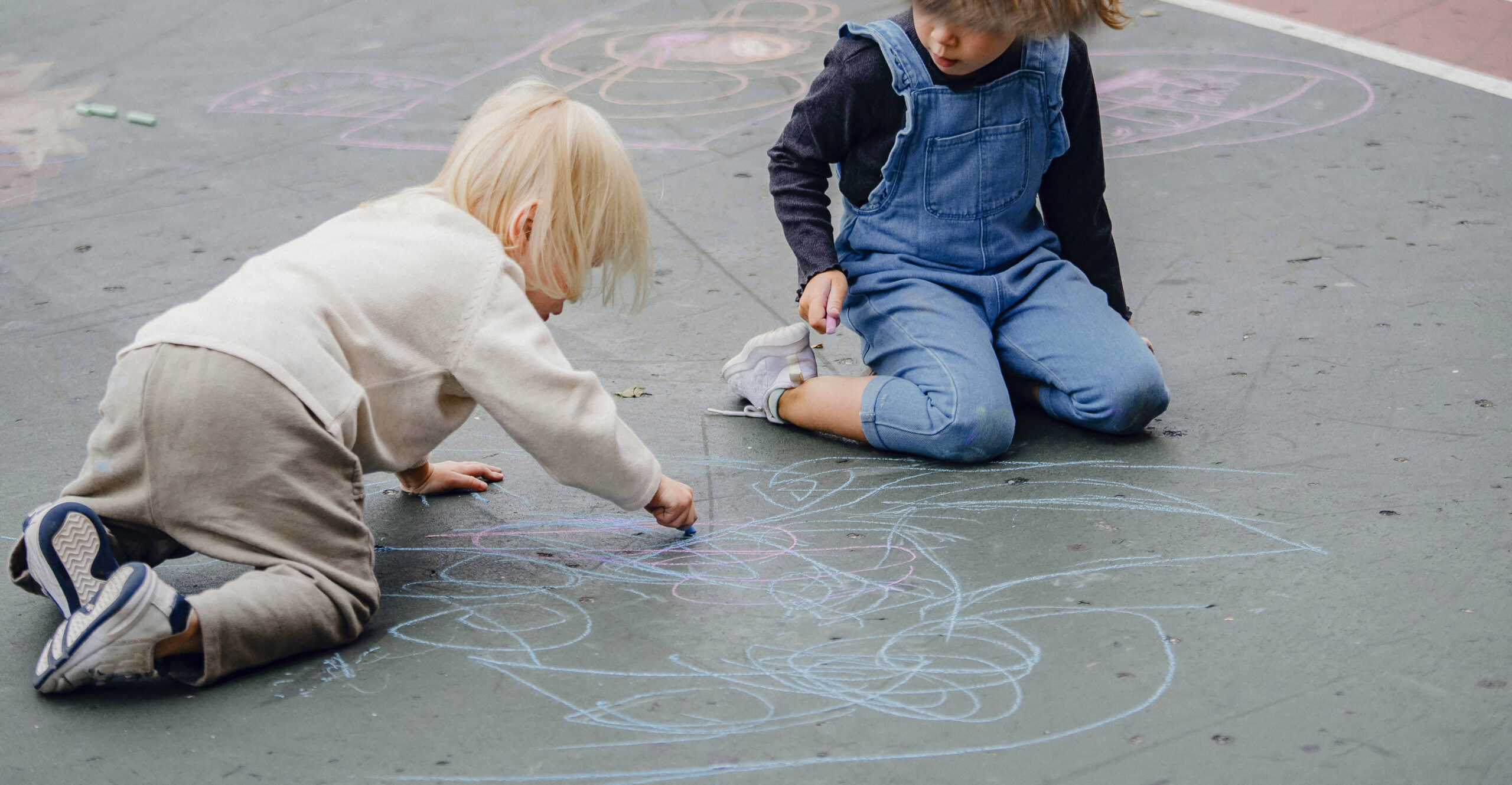 two children drawing on the road with chalk