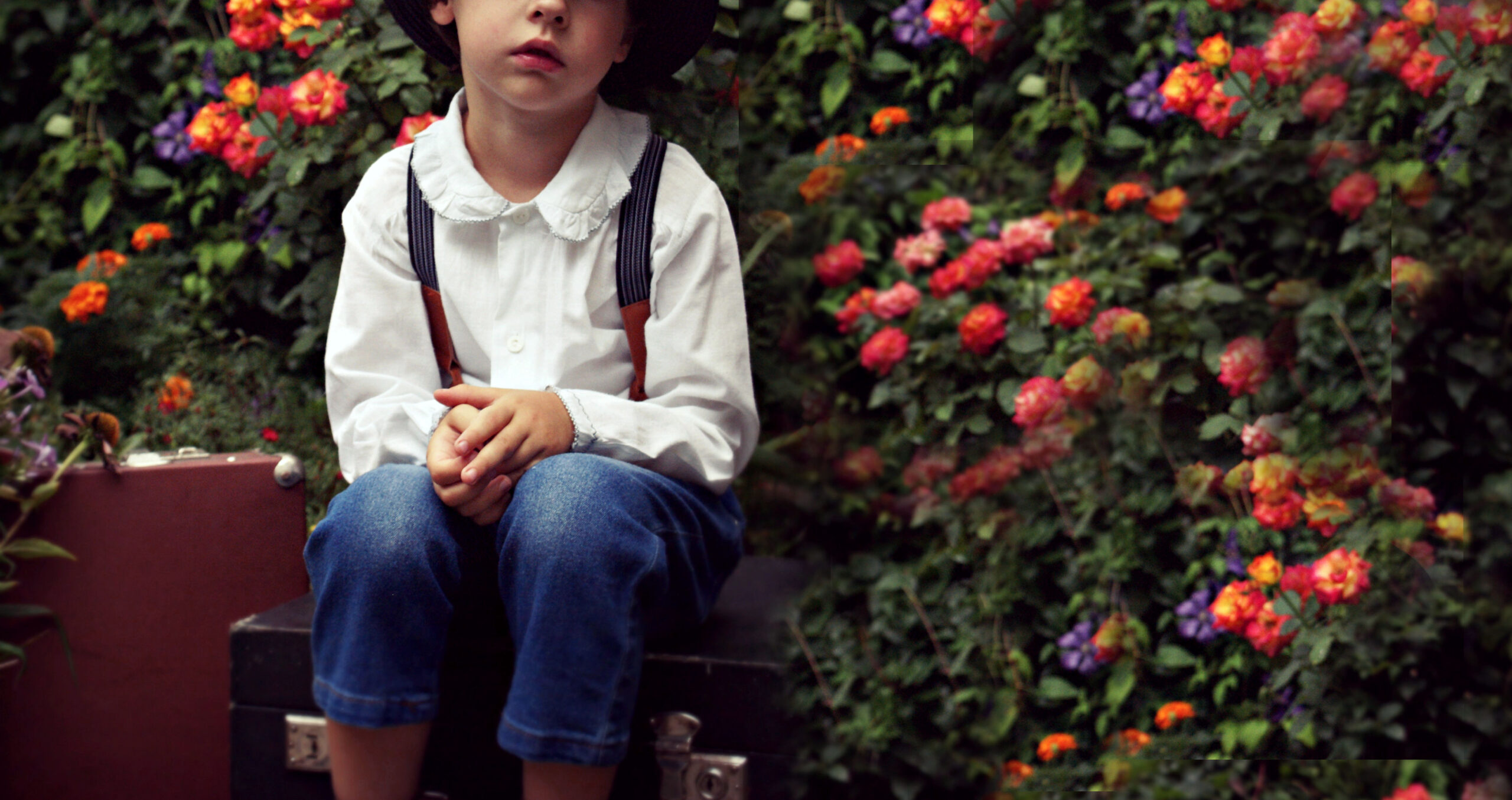 a child sitting in front of a hedge of flowers