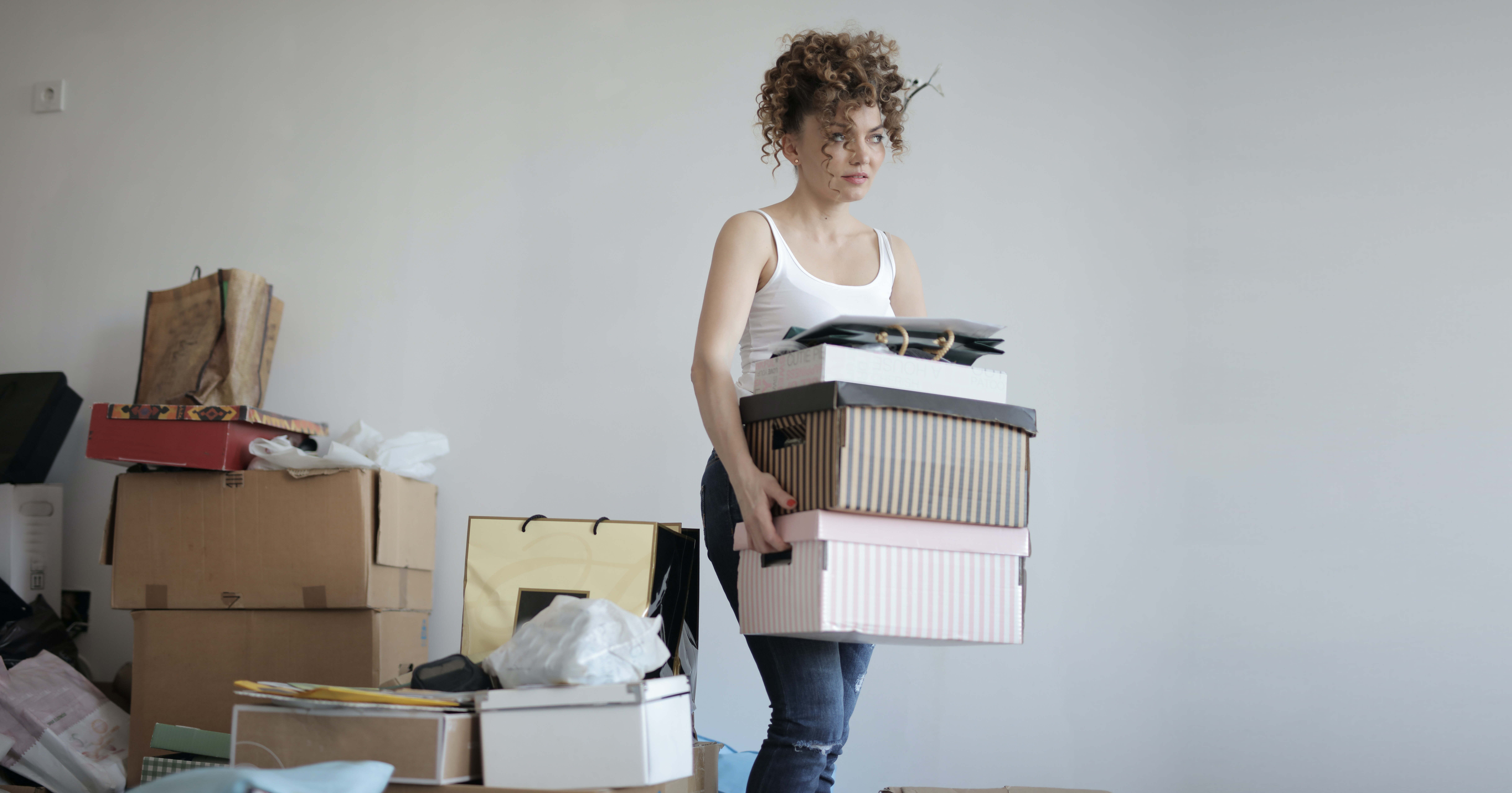 a woman carrying boxes in a chaotic messy room