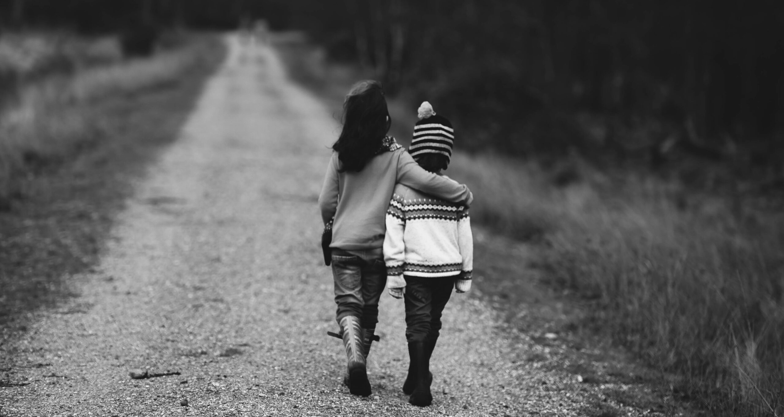 two children walking away arm-in-arm along a road - black and white image