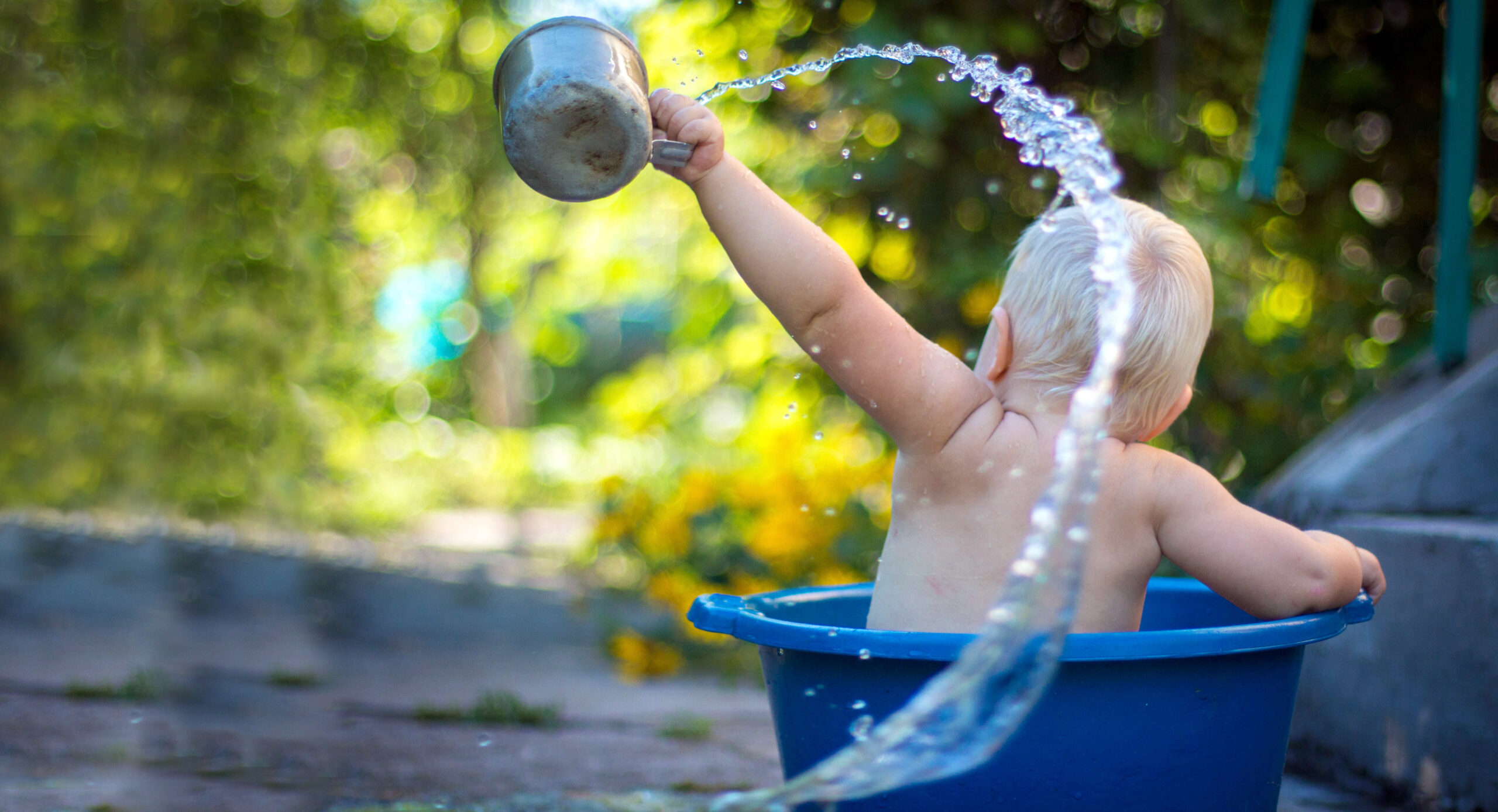 toddler sitting in a large bowl outside, playing with water