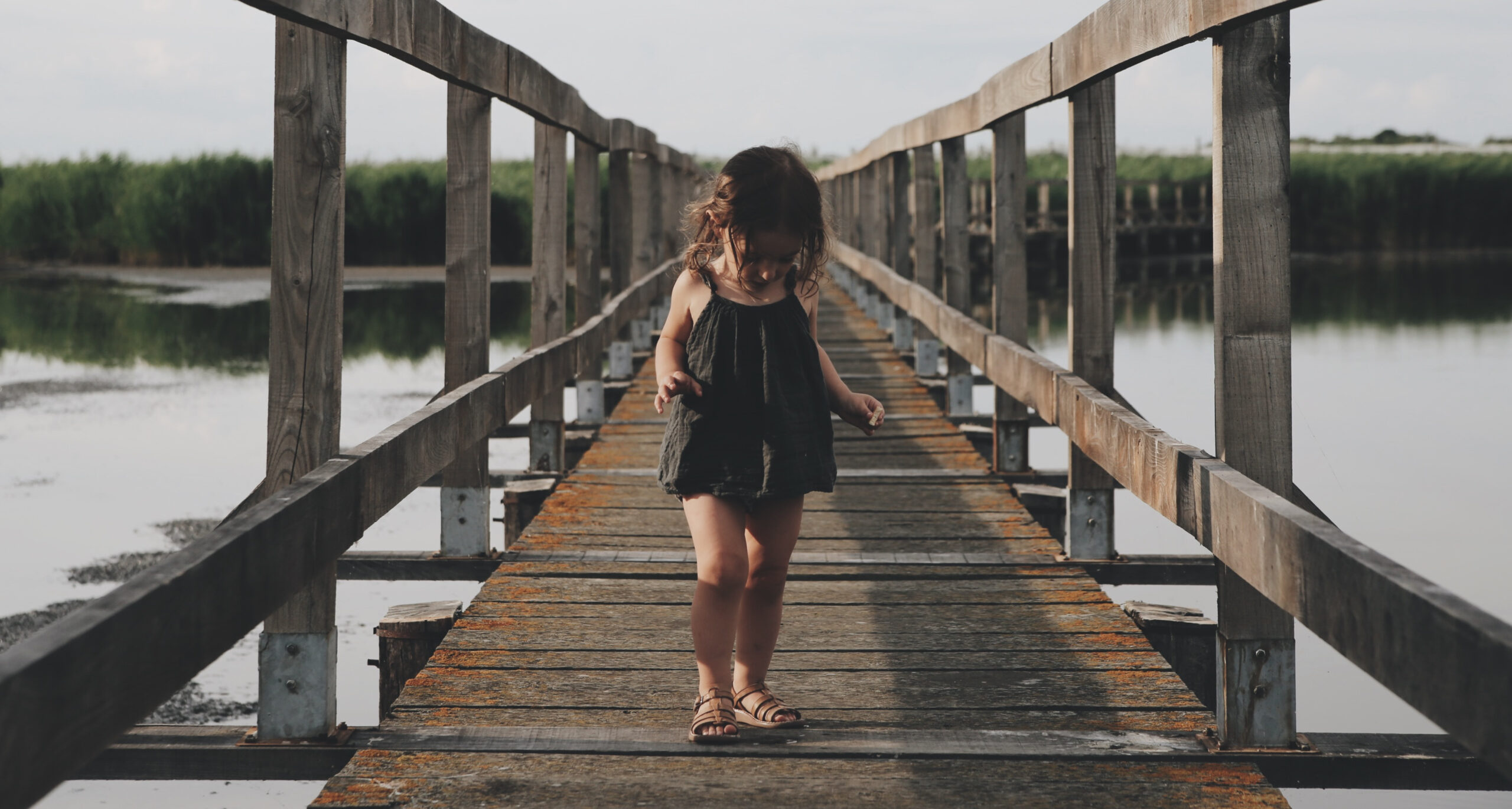 a child standing alone on a wooden walkway over water