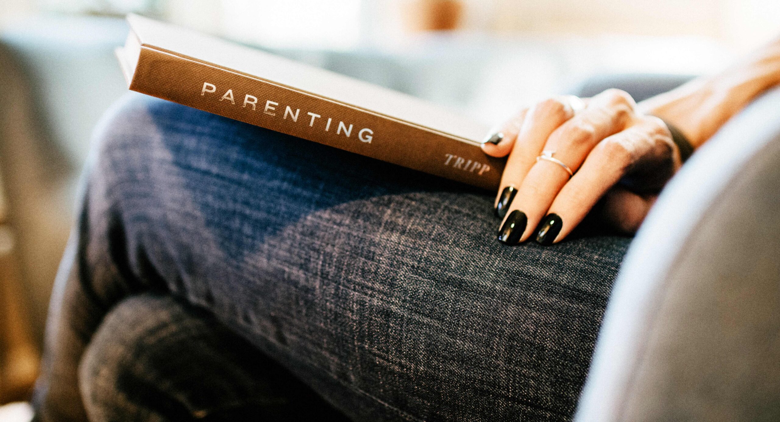 Someone sitting with a book on her lap, the word "parenting" on the spine of the book.