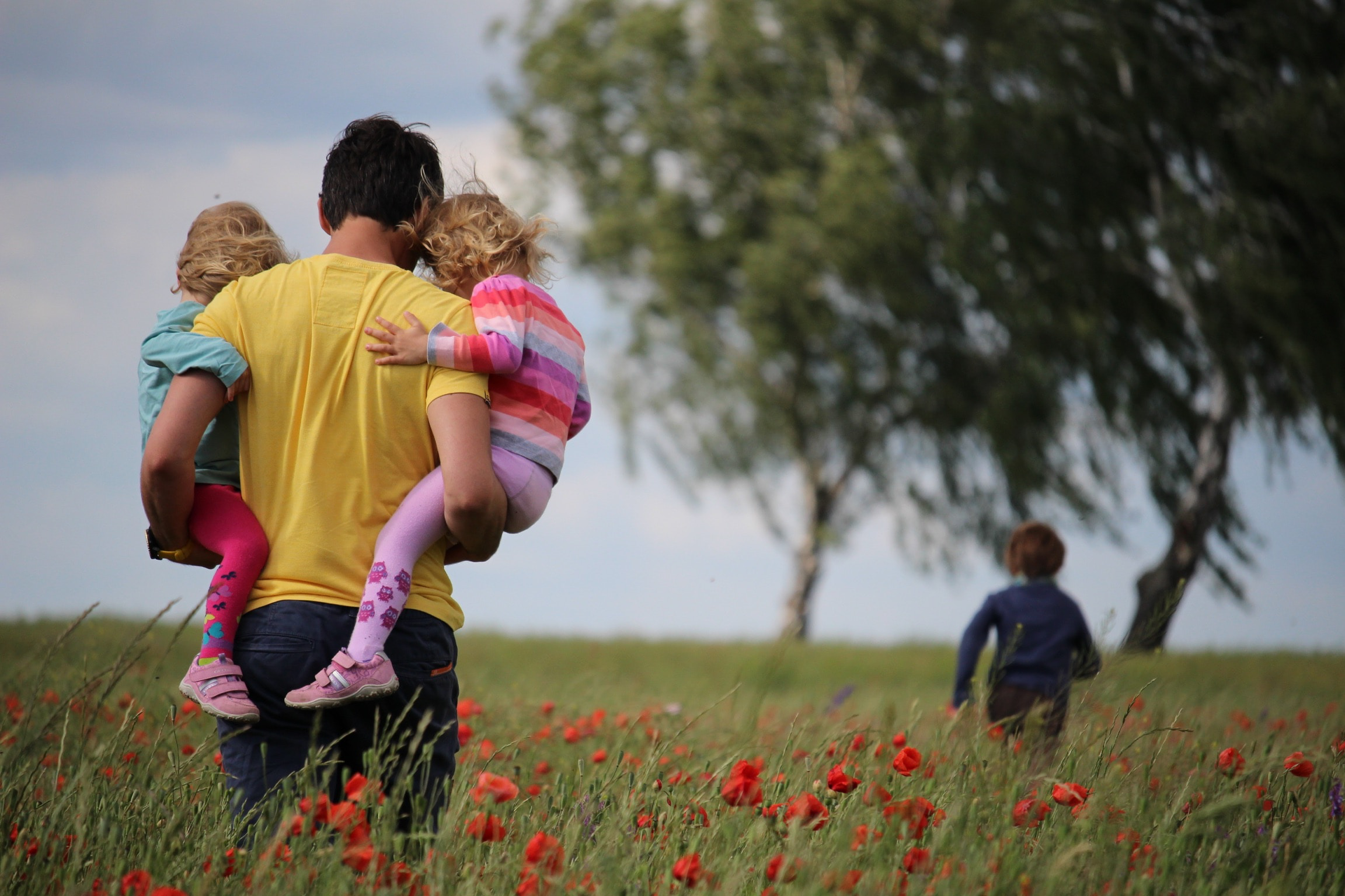 a father carrying his two children in a field of poppies
