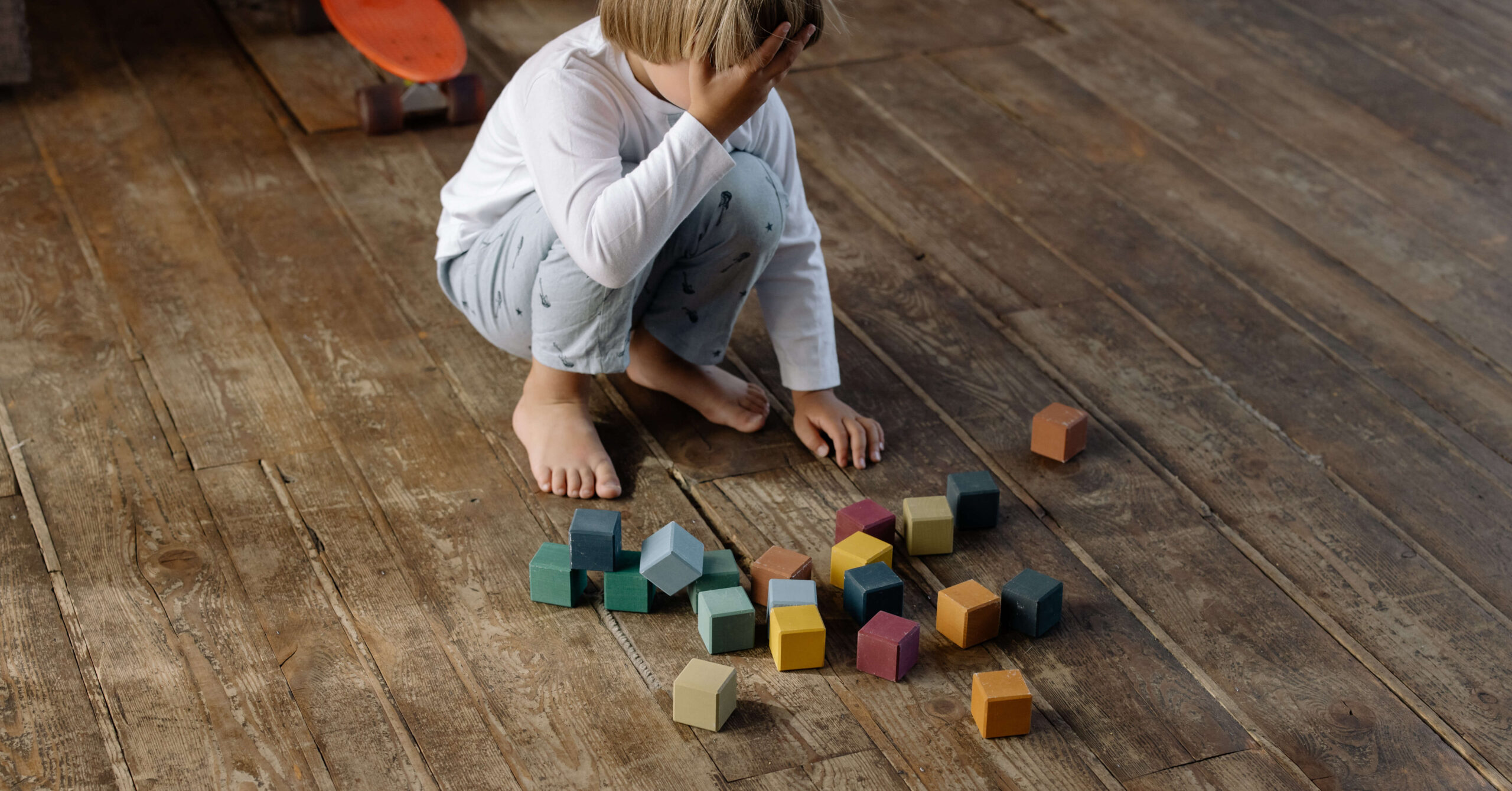 a child looking upset, squatting on the floor with blocks