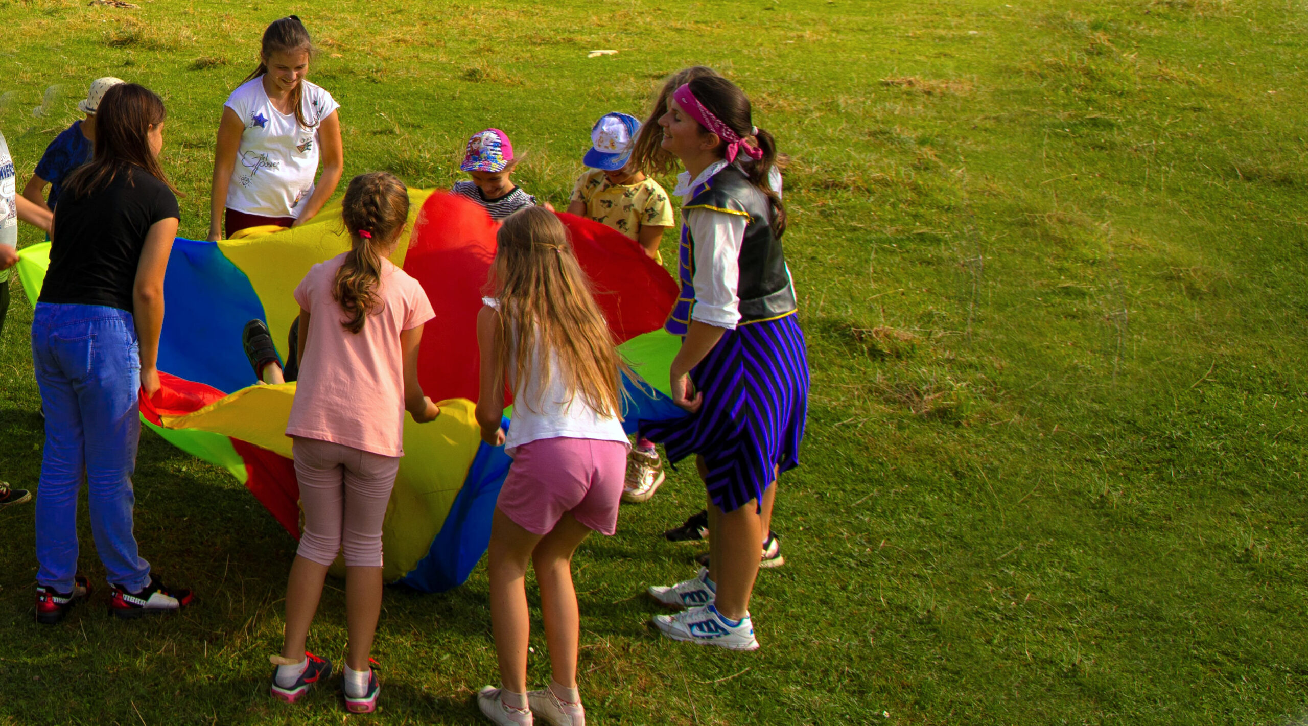 a group of adults and children in a park, holding a large, colourful groundsheet