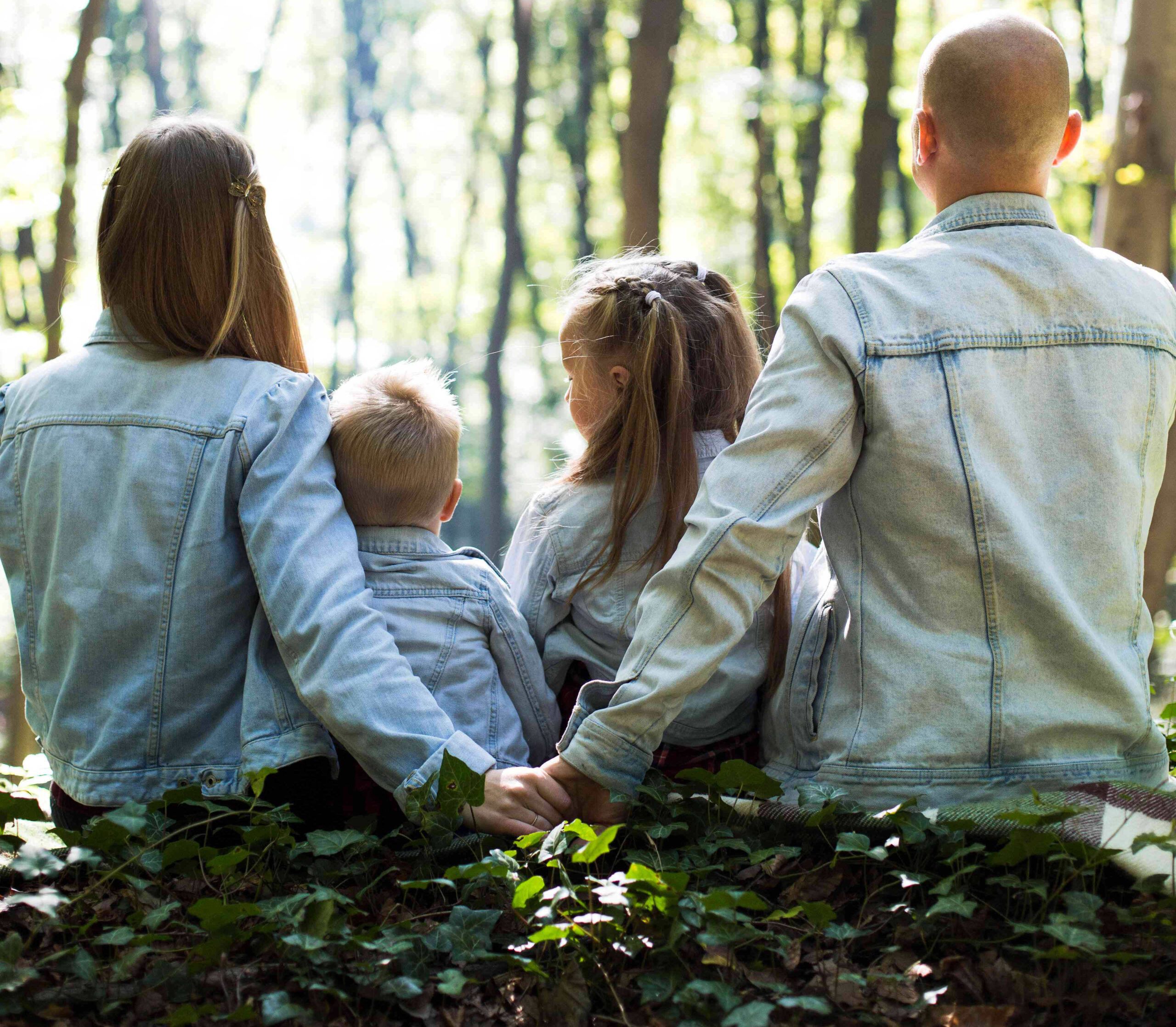 a family sitting in the woods, the parents holding hands behind their children