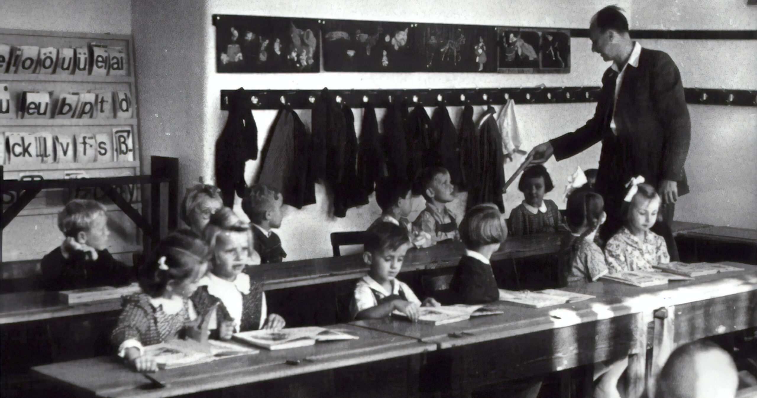 a historical photo of a teacher and children in a schoolroom