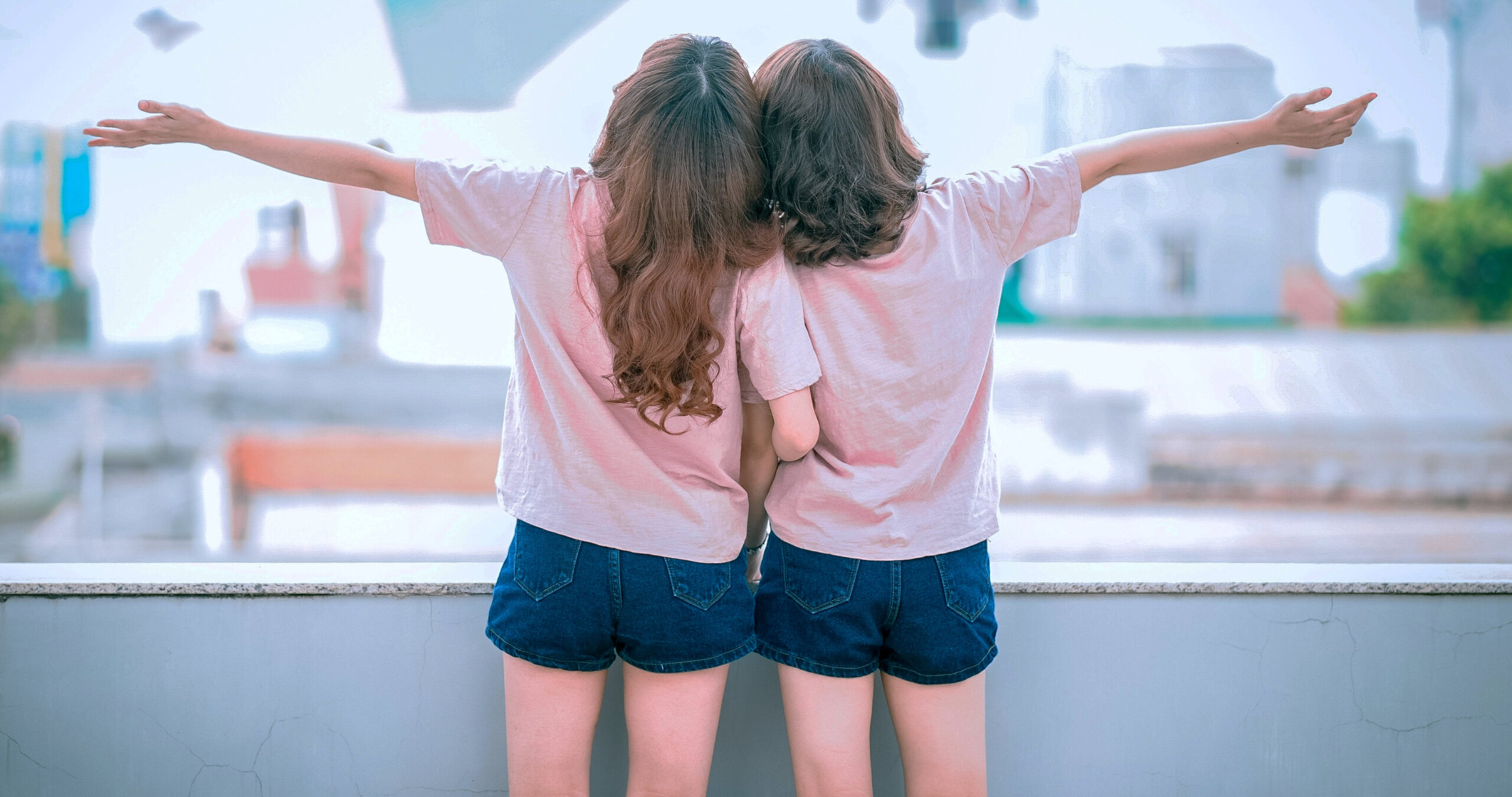 two girls standing with heads together, arms out, happy, connecting