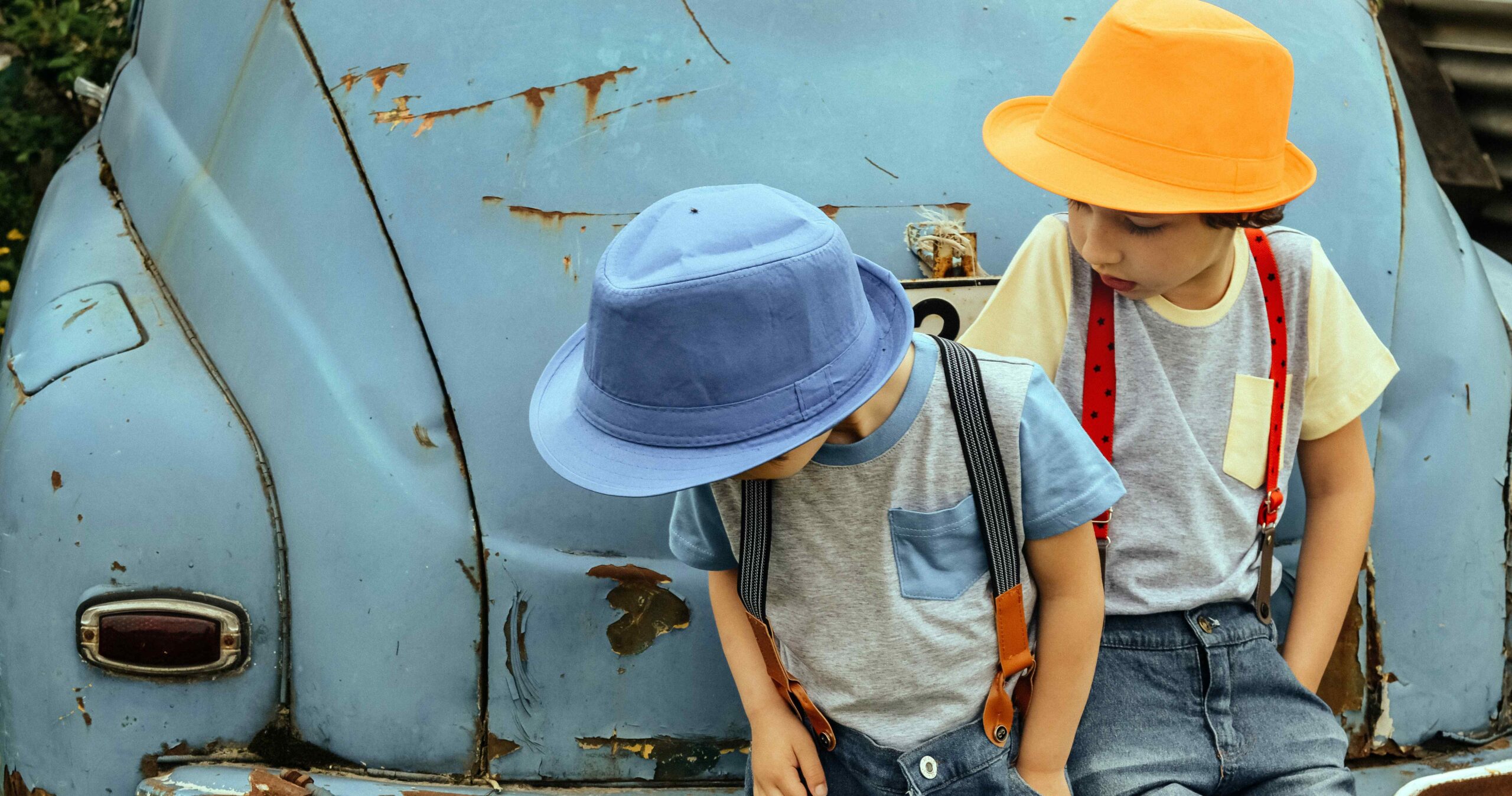 children sitting against a rusty car